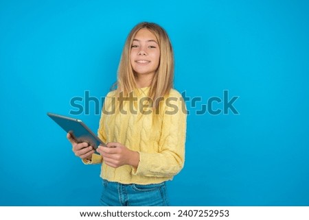 Photo of optimistic Beautiful kid girl wearing yellow sweater hold tablet