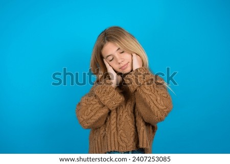 Pleased Beautiful kid girl wearing brown knitted sweater enjoys listening pleasant melody keeps hands on stereo headphones closes eyes. Spending free time with music