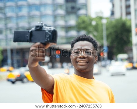 Young African American man influencer doing a live with a camera in a city