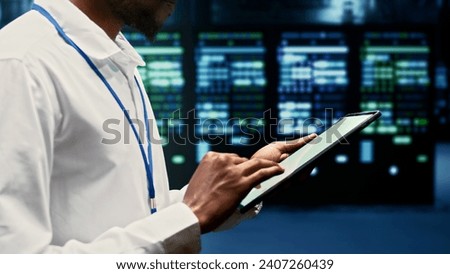 Skilled worker walking through supercomputers delivering web content to online customers. Repairman in server room using tablet to make sure critical systems are working errorless, close up