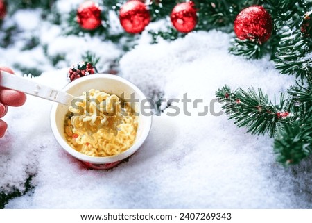 a cup of instant noodles that have been brewed with a backdrop of winter scenery, snow and trees around it