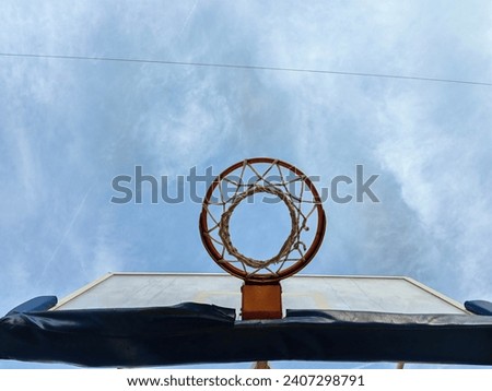 Basketball  orange hoop with net and glass backboard , against blue sky with clouds. Low angle perspective.