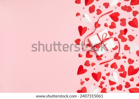 Valentine or Mother day festive border composition with gift or present box and many red hearts on pastel pink background top view. Flat lay greeting card.