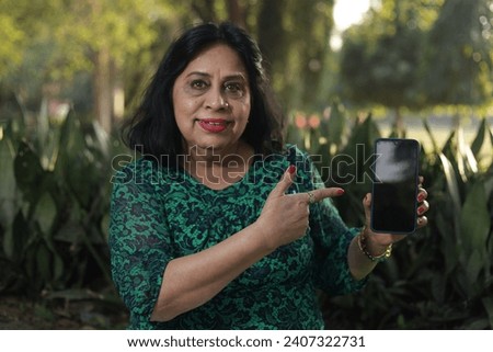 Woman Showing Cell phone Empty Screen Recommending Application Standing Outside. Shallow Depth, Mockup. pointing towards screen.