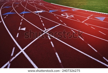 A red artificial surface running track. A sports ground. Painted marked lines for lanes.