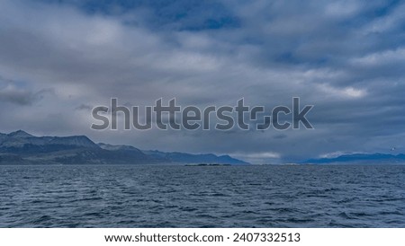 A calm seascape. Ripples on the surface of the blue ocean. Clouds in the azure sky. The Andes mountain range in the distance. Argentina. Beagle Channel. Tierra del Fuego Archipelago