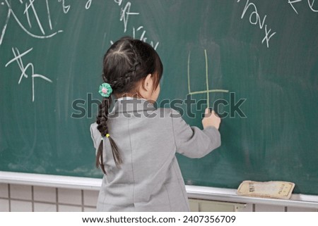 Little girl practices writing with chalk on blackboard while visiting classroom