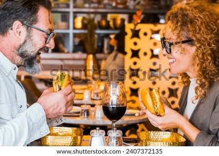 Happy couple smiling and talking in a pub restaurant eating burgers and chips - Married couple having lunch break at cafe bar - Lifestyle concept with man and a woman going out on weekend day