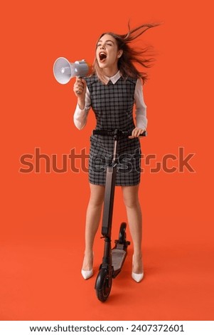 Portrait of young businesswoman with megaphone riding kick scooter on orange background