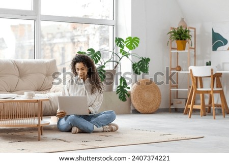 Young African-American woman using laptop on floor at home