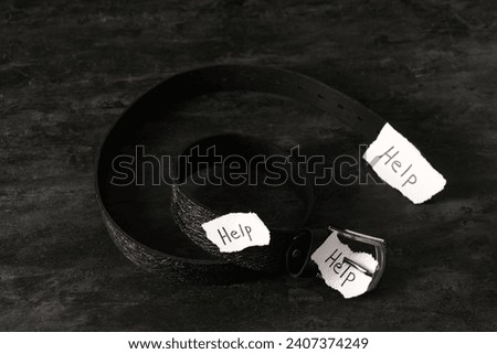 Paper pieces with word HELP and belt on dark background. Domestic violence concept