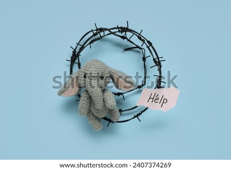 Paper piece with word HELP, barbed wire and toy elephant on blue background. Domestic violence concept