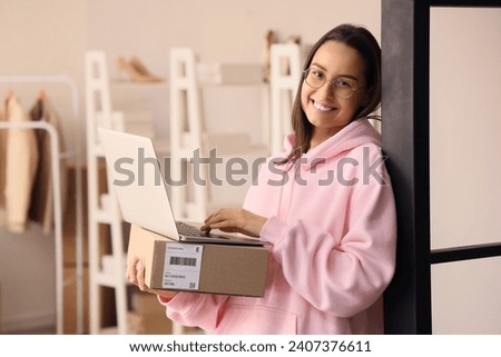 Female seller with parcel using laptop in warehouse store Royalty-Free Stock Photo #2407376611