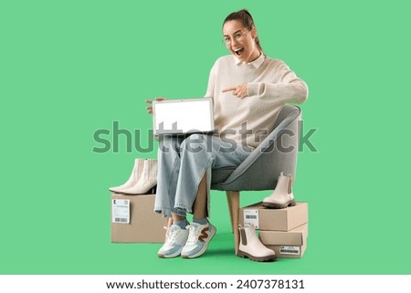 Female seller with parcels pointing at laptop in armchair on green background Royalty-Free Stock Photo #2407378131