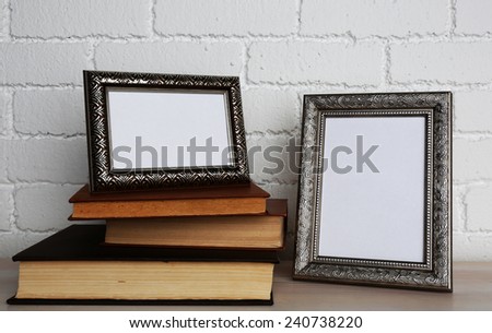 Golden photo frames with books on wooden surface, on brick wall background