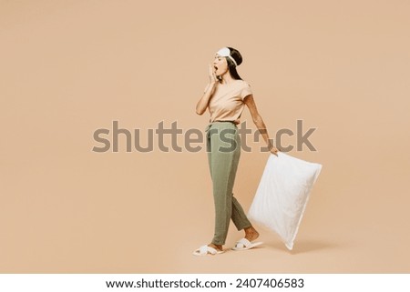 Full body young calm Latin woman she wears pyjamas jam sleep eye mask rest relax at home walk go hold pillow cover mouth with hand yawn isolated on plain beige background. Good mood night nap concept Royalty-Free Stock Photo #2407406583