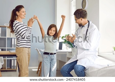 Male pediatrician and happy mother applaud little girl during appointment in medical office. Preteen girl celebrates successful completion of treatment. Medicine, healthcare and pediatry concept. Royalty-Free Stock Photo #2407418405