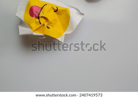 Square piece of paper with the face of a mocking emoji with tongue out.