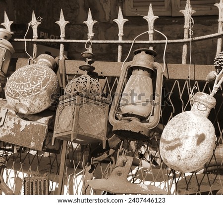 An assortment of aged utensils showcasing signs of rust and peeling paint. Along the fence, lanterns and flags sway, creating a festive ambiance on a cheerful and sunny day. The scene unfolds outdoors