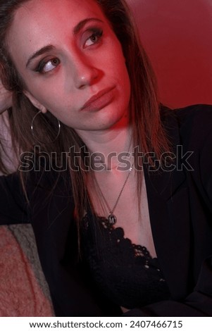 Handsome Italian Caucasian woman dressed well posing for photo shooting. The girl looks to the photographer illuminated with a red light. Concept of beauty and determination long hair