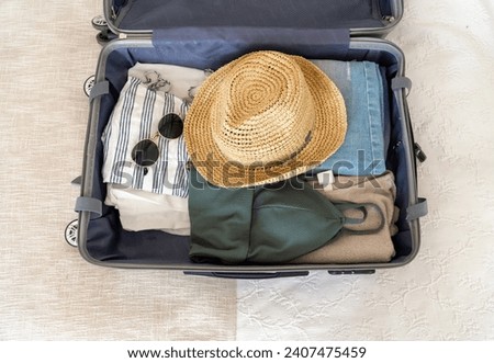 Open suitcase with neatly folded clothes, sunglasses, and hat ready for the trip.