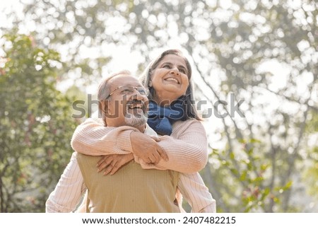 Carefree senior man piggybacking playful wife in park Royalty-Free Stock Photo #2407482215