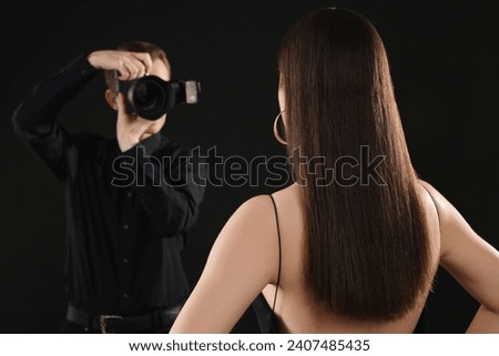 Professional photographer taking picture of model on black background, selective focus