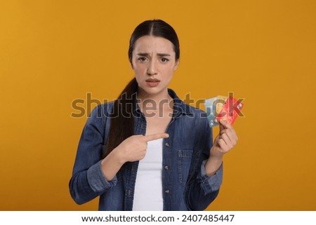 Confused woman pointing at credit cards on orange background. Debt problem