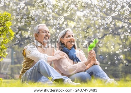 Senior couple having fun blowing bubbles at park Royalty-Free Stock Photo #2407493483