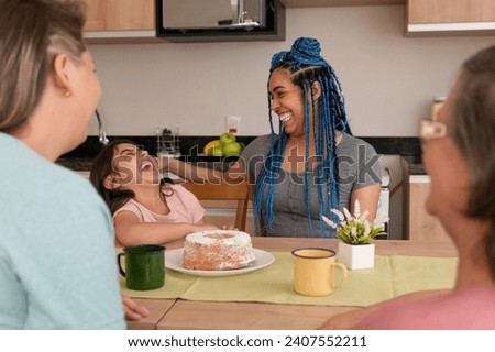 Happy cheerful adopted young child with enthusiasm laughing with her parents and grandmother in kitchen home, indoors. Lgbtq family, happiness, affection, love, care concept. Royalty-Free Stock Photo #2407552211