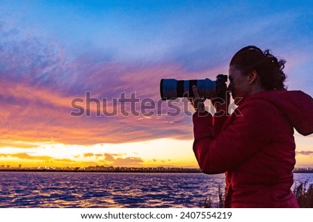Woman photographing seascape at sunset with professional camera.