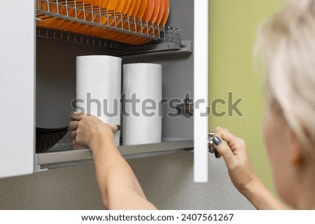 a woman's hand takes out a paper towel from the closet. housewife takes out a roll of paper towel from the kitchen cabinet. High quality photo Royalty-Free Stock Photo #2407561267