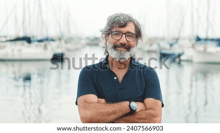 Happy male seigneur in glasses crossing his arms while standing in the port and looking at the camera on yachts background, camera is moving closer Royalty-Free Stock Photo #2407566903