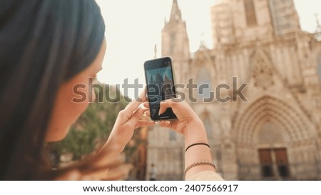 Traveler girl, with backpack on her shoulders, takes photo on mobile phone of an old building in the historical part of European city, back view