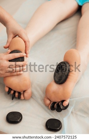 Health masseur makes a foot massage with stones to the client in the office