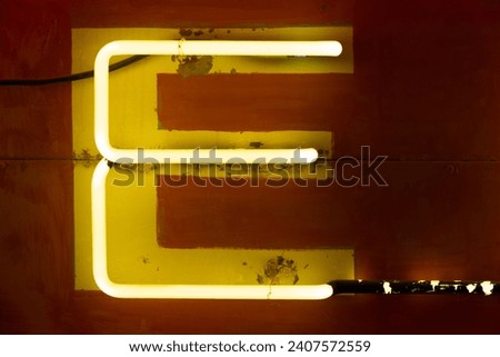 Neon yellow E letter illuminated on a sign at night