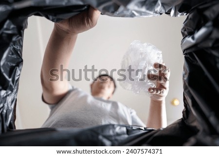 Image from inside black recycling bag of man throwing empty plastic bottle in recycling bin Home recycle eco green zero concept  Royalty-Free Stock Photo #2407574371