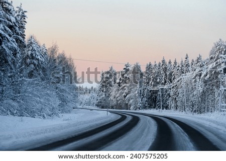 Finland - December 31 2023: Snowy road in Lapland. Sunset colors the sky, frosty trees on the road side. Temperature outside is around minus 25 degrees Celsius.
