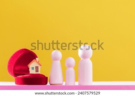 Home model and red gift box and wood family put on the pink foam on bright yellow color background in the office, The buying a new real estate as a gift to one loved concept.
