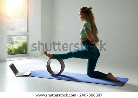 young flexible girl doing gymnastics, flexibility and stretching using a yoga wheel online on a white background