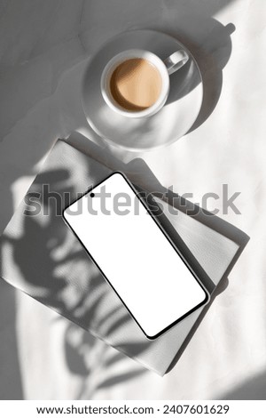 Minimal aesthetic business branding or social media template. Mobile phone with empty white screen mockup, gray notebook, cup with milky coffee on marble table background with natural sunlight shadows