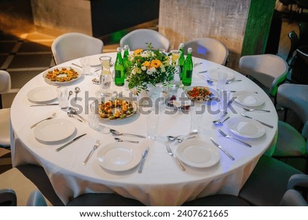 beautifully arranged round banquet table set for a formal dining event. The table is dressed with a crisp white tablecloth and is set with white plates, silverware, and clear glasses
