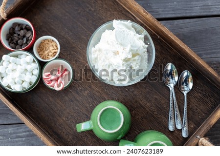 Hot chocolate bar concept. 3green mugs with bowl of whipped cream and toppings in different holiday bowls; mini marshmallows, chocolate chips, miniature candy canes, toffee pieces, on a wood tray. Royalty-Free Stock Photo #2407623189