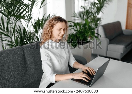 young focused freelancer working with notebook in cafe, typing text and smiling, concentrated caucasian blonde businesswoman in white shirt, green plants in background, freelance concept