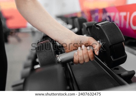 two rows of black dumbbells in fitness gym, sport equipment, hand of athletic caucasian woman holds one dumbbell for training, selective focus