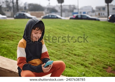 Teenage hipster boy in trendy sports clothes, sitting on steps and using smart phone, checking social media content or playing online video games. People. Mobile application, Technology. Copy ad space