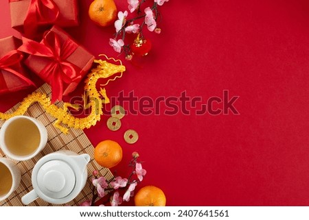 Chinese New Year tea ceremony idea. Top view shot of teapot, cups of tea, gold dragon, tangerines, red gift boxes, traditional chinese decor on red background with promo area