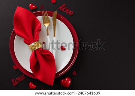 Creating unforgettable memories over a romantic dinner on Valentine's Day. Top view shot of plates, cutlery, hearts, red napkin on black background with advertisment area Royalty-Free Stock Photo #2407641639
