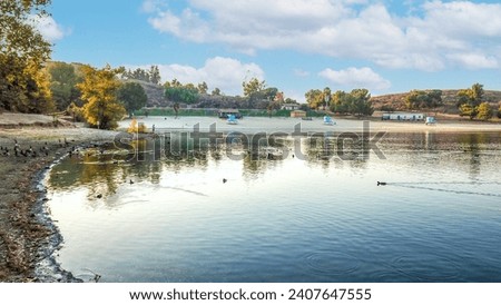 an aerial shot of a beautiful summer landscape at Puddingstone Lake with lush green trees and plants reflecting off the water, majestic mountain ranges with homes at sunset in San Dimas California USA Royalty-Free Stock Photo #2407647555