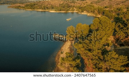 an aerial shot of a beautiful summer landscape at Puddingstone Lake with lush green trees and plants reflecting off the water, majestic mountain ranges with homes at sunset in San Dimas California USA Royalty-Free Stock Photo #2407647565